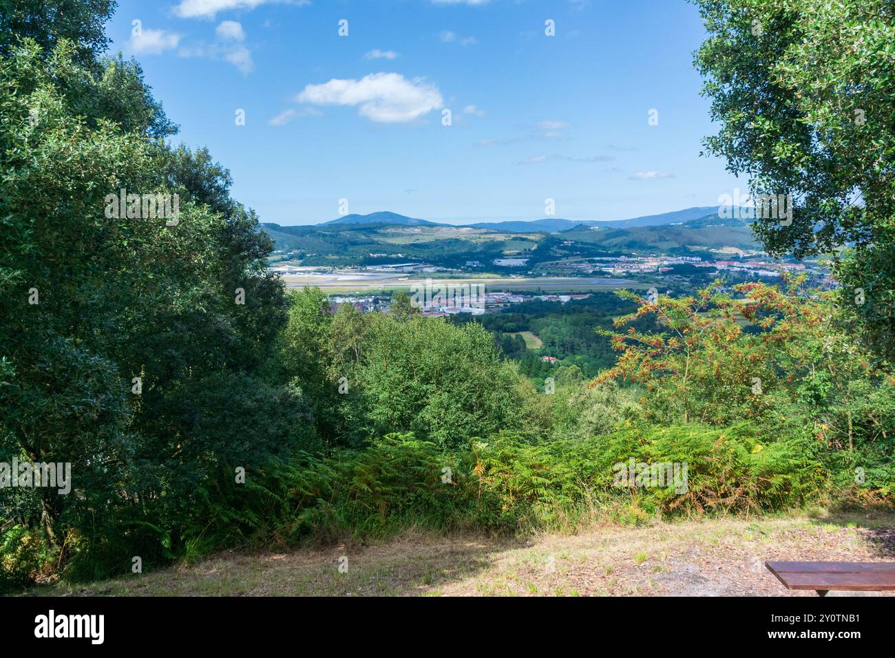 Blick auf einen Flughafen durch Bäume in der Nähe von Bilbao im Sommer gegen Berge und Himmel Stockfoto