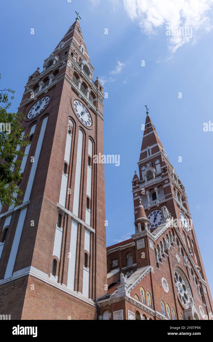 Die beiden Türme der Szeged-Votivkirche - Szeged-Kathedrale - in Ungarn an einem sonnigen Tag mit blauem Himmel und Blick auf die Uhr auf dem Turm. Stockfoto