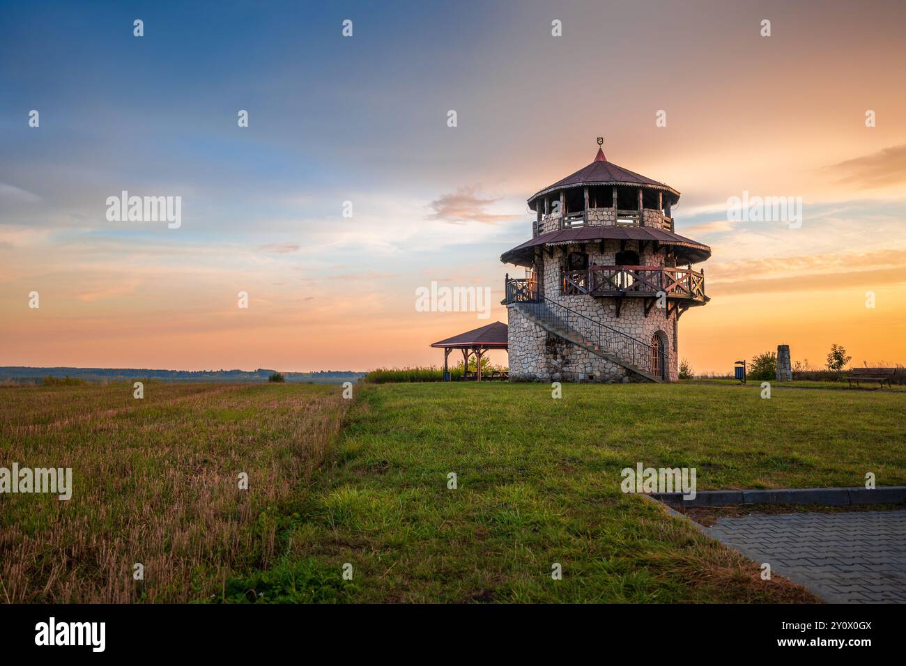Ein wunderschöner Aussichtsturm aus Stein vor dem Hintergrund einer wunderbaren Landschaft bei Sonnenuntergang. Mehrfarbiger, heißer Himmel. Susiec, Roztocze, Polen Stockfoto