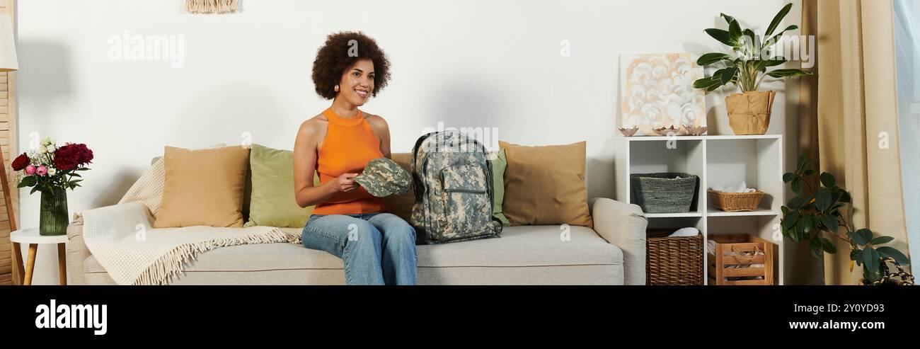 Eine junge Frau genießt einen gemütlichen Moment in ihrem Wohnzimmer, umgeben von Dekor und ihrem Militärrucksack. Stockfoto