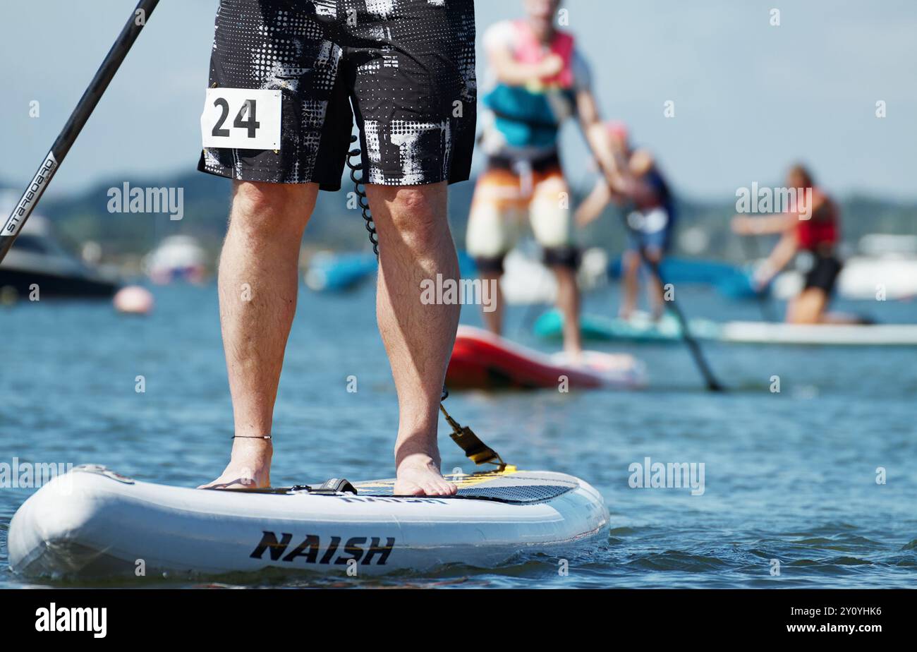 Die Beine Eines Teilnehmers in einem Amateur, Fun, Stand Up Paddleboard Race gefolgt von anderen Teilnehmern im Hintergrund, Mudeford, Großbritannien Stockfoto