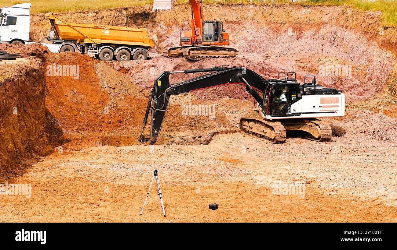 Eine Baustelle mit Baggern und einem Kipplaster, der an einer Ausgrabung arbeitet, Konzeptfotos der Rohkraft von Maschinen sowie Arbeitsthemen, Stockfoto
