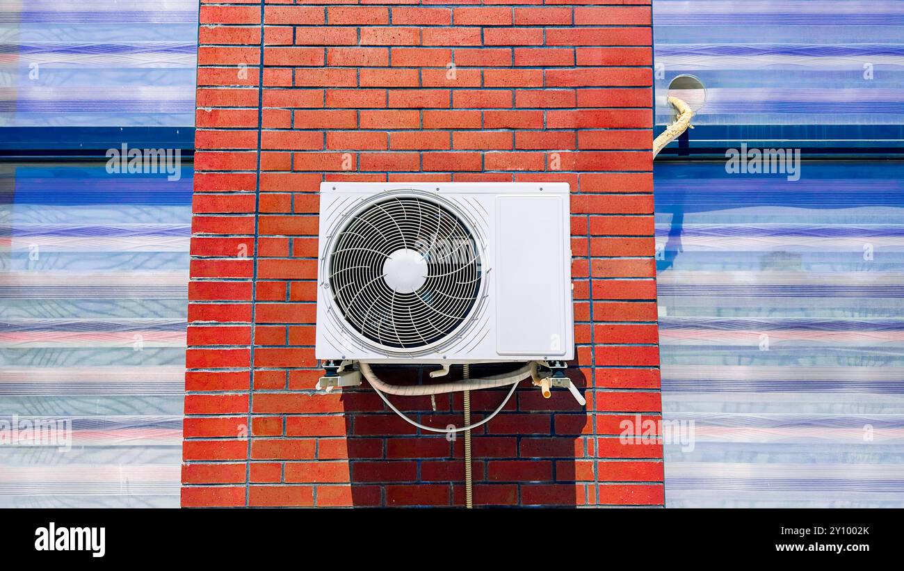 Nahaufnahme einer an einer Ziegelwand montierten Außenklimaanlage. Moderne Technologie in energieeffizienten Kühl- und Lüftungssystemen Stockfoto