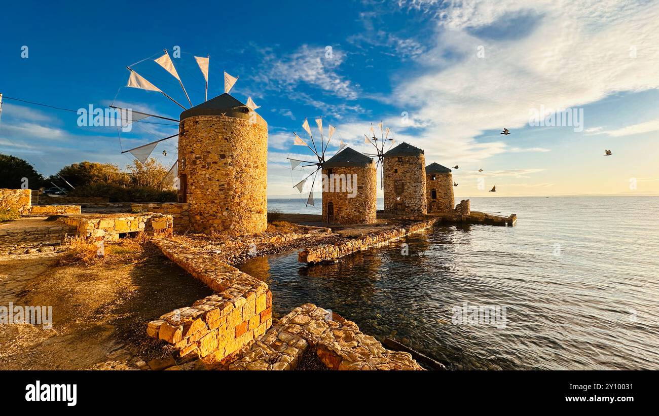 Alte Windmühlen am Meer bei Sonnenuntergang auf der Insel Chios, Griechenland. Wecken Sie Ruhe und Nostalgie in dieser malerischen Küstenszene. Stockfoto