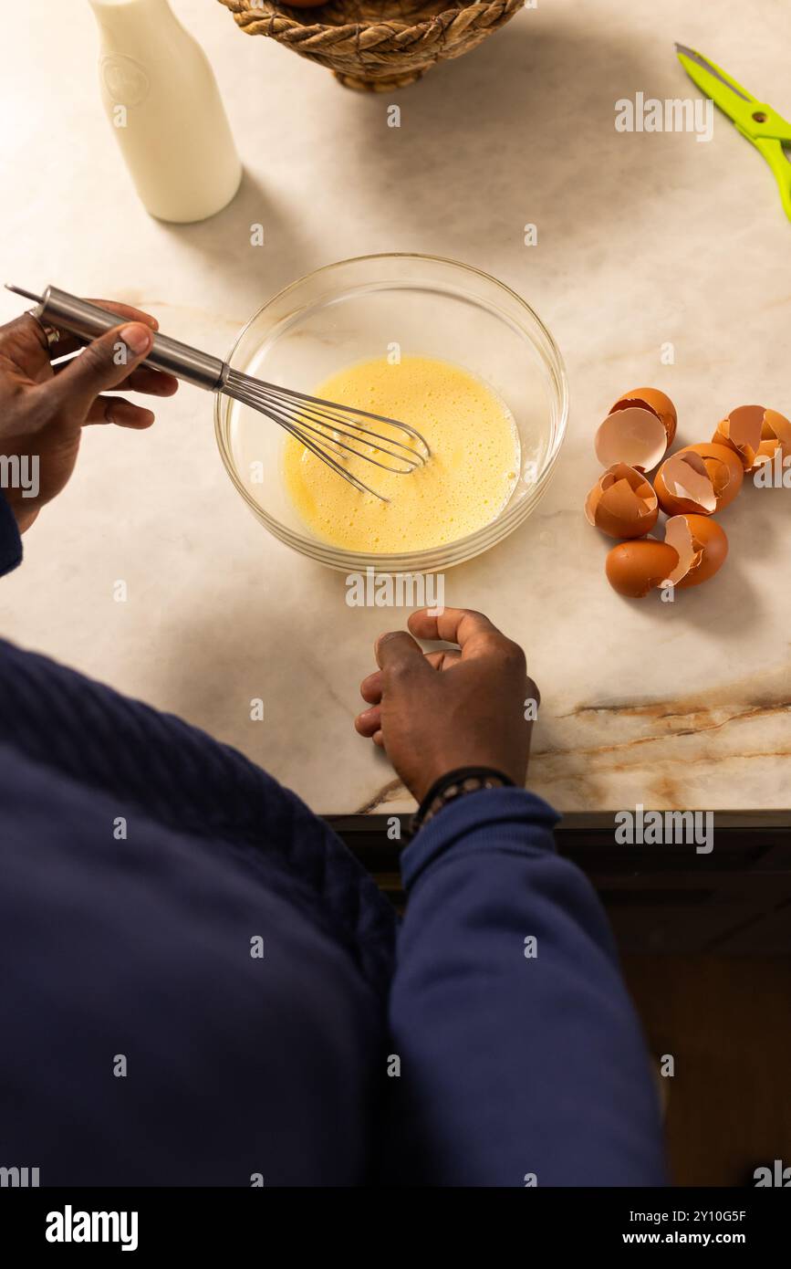 Eier in einer Glasschale rühren, ein afroamerikanischer Mann bereitet Zutaten für das Kochen in der Küche vor Stockfoto