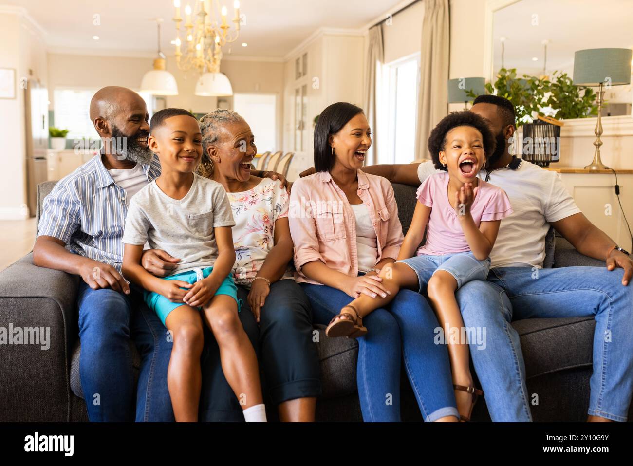 Lächelnde, generationsübergreifende Familie sitzt auf der Couch und genießt die gemeinsame Zeit zu Hause Stockfoto