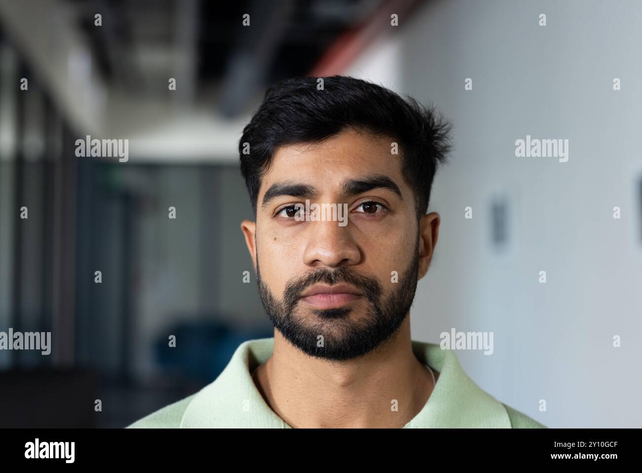 Indischer Mann im Amt, der mit ernstem Ausdruck in die Kamera schaut und ein grünes Hemd trägt Stockfoto