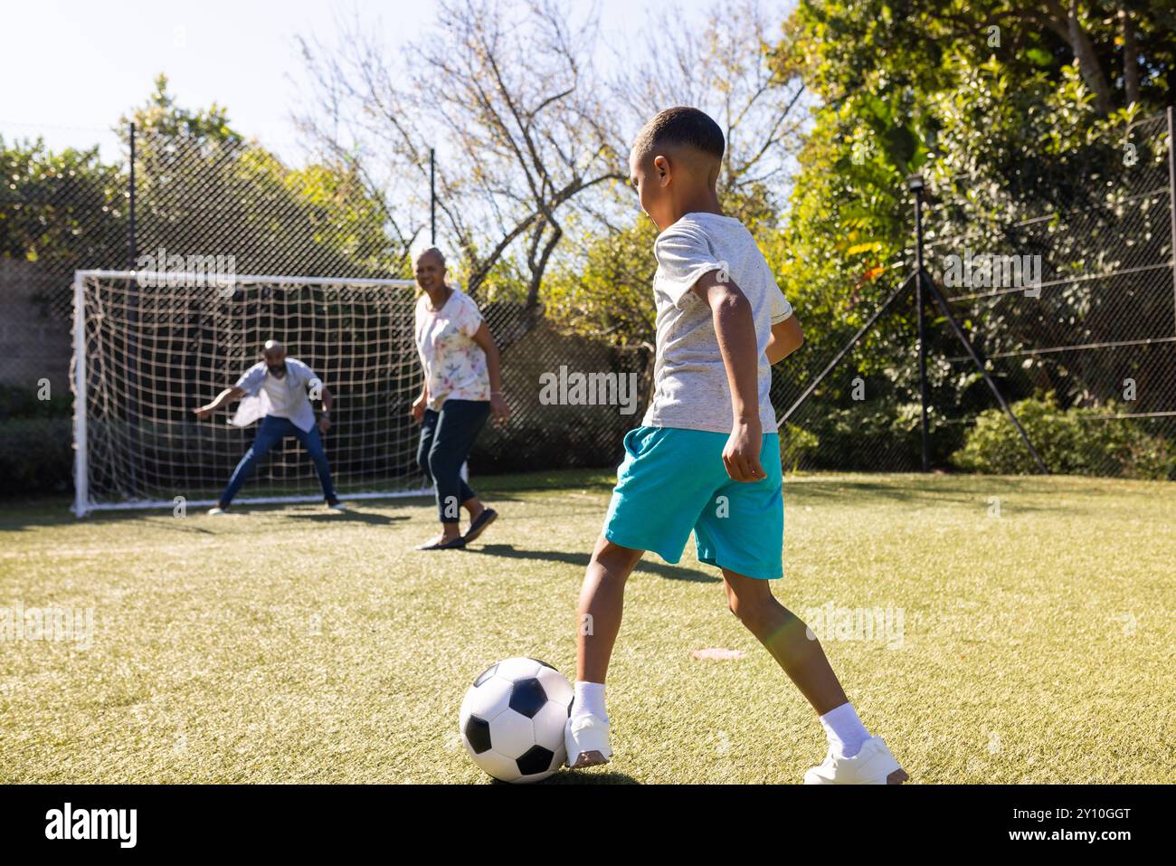 Fußball im Freien spielen, Junge mit dem Ball ins Tor treten, Großeltern und Enkel beobachten Stockfoto