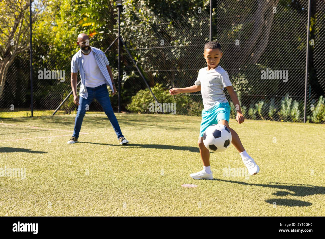 Fußball spielen, Enkel kickt Ball, während Großvater auf dem Feld zusieht Stockfoto
