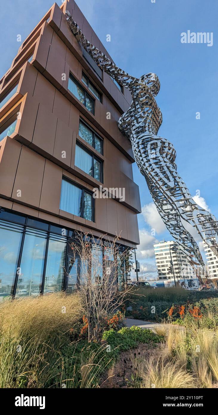 Amsterdam, Niederlande - 15. März 2024: Markante Skulptur aus Metall in menschlicher Form, die die moderne Gebäudefassade mit landschaftlich gestaltetem Vordergrund und urbanen n ziert Stockfoto Amsterdam, Niederlande - 15. März 2024: Markante Skulptur aus Metall in menschlicher Form, die die moderne Gebäudefassade mit landschaftlich gestaltetem Vordergrund und urbanen n ziert Stockfoto