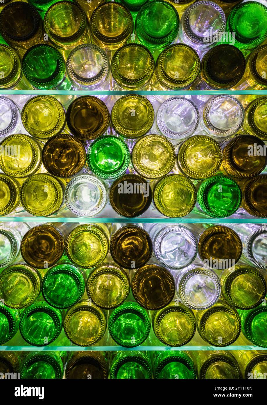 Natürlich beleuchtete, mehrfarbige Weinflaschen auf Glasregalen Stockfoto