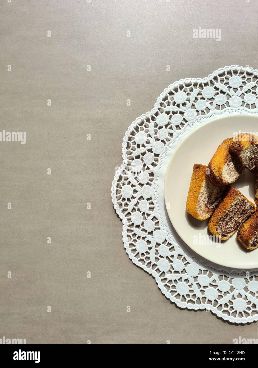 Einzelne Marmorkuchen auf einem weißen Teller auf einer runden dekorativen Papierkuchenauflage auf grauem Hintergrund serviert Stockfoto