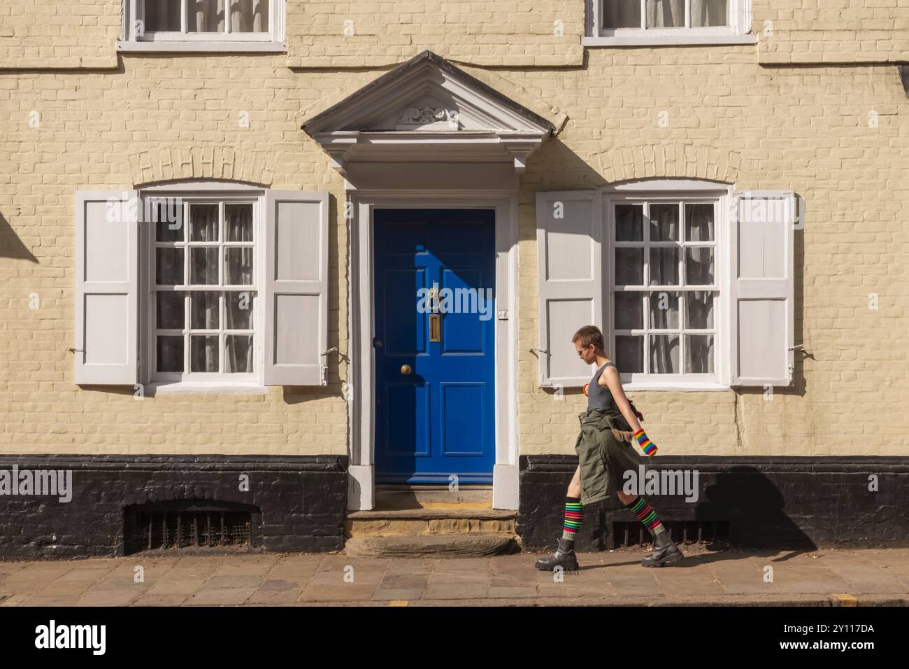 England, Kent, Canterbury, die High Street, Young Woman, die an einem Gebäude aus der georgianischen Zeit vorbeiläuft, mit blauer Tür und Fensterläden Stockfoto