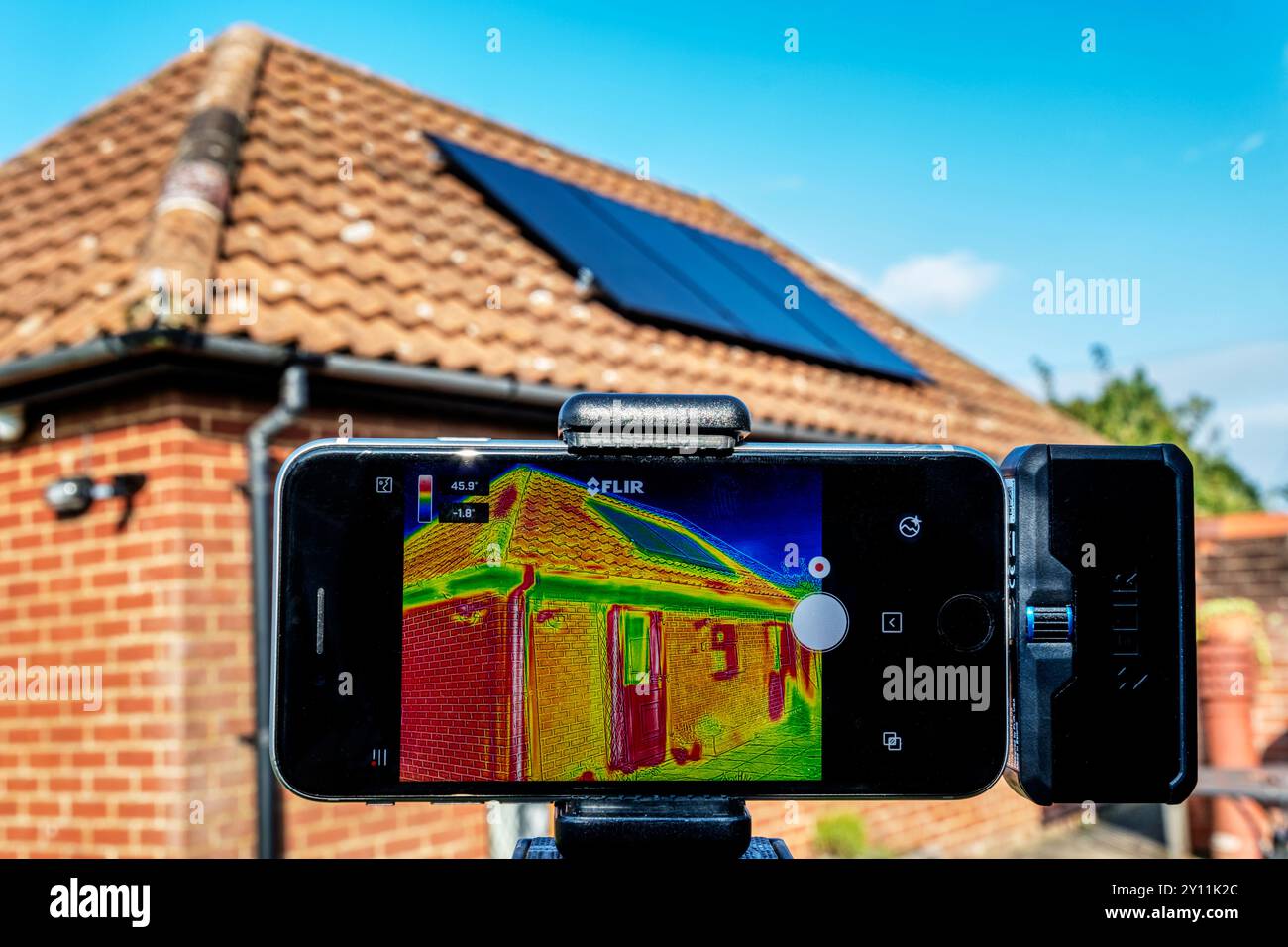 Eine Infrarot-Thermografie, die zur Beurteilung des Wärmeverlustes eines Bungalows mit Solarpaneelen auf dem Dach verwendet wird. Stockfoto