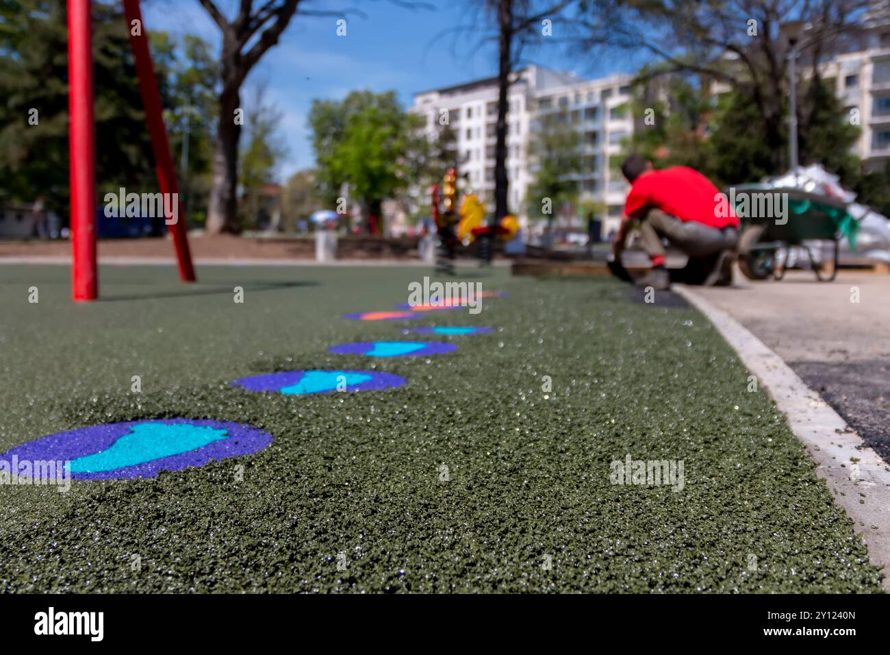 Neuer Kinderspielplatz im Bau. Eine maurerhand mit Kelle verteilen und glätten weichen Gummibröseln Gummimulch für Kinder Spielzeuge Stockfoto