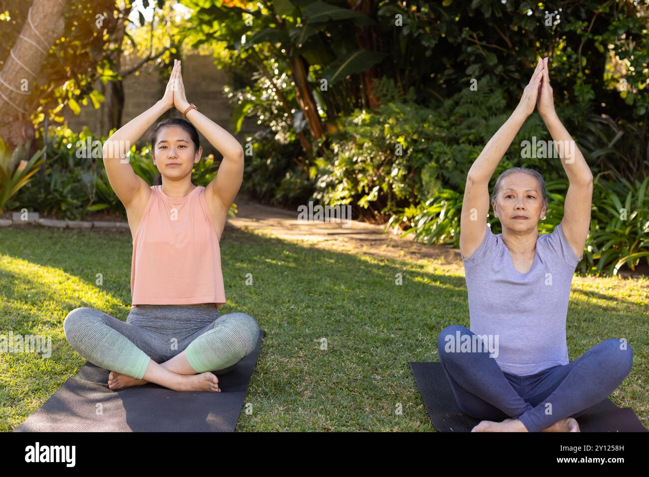 Yoga üben, asiatische Großmutter und Enkelin sitzen auf Matten im Garten und meditieren zusammen Stockfoto