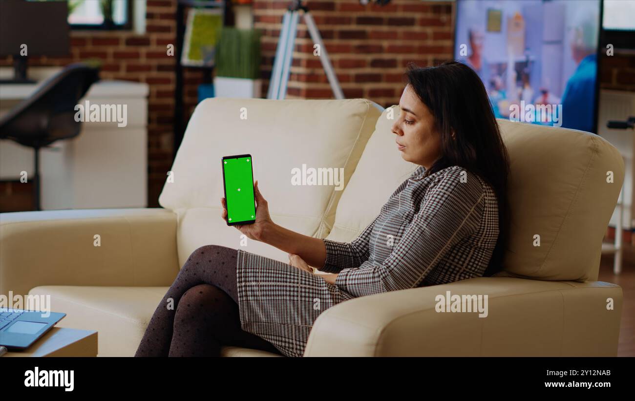 Person, die während der Arbeit von zu Hause aus E-Mails auf dem Mobiltelefon mit grünem Bildschirm abruft. Indische Frau in gemütlicher Wohnung, die Aufgaben erledigt, Geschäftsnachrichten auf dem Mockup-Handy liest, Schuss schießt Stockfoto