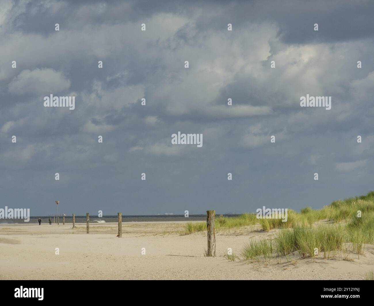 Ein langer Strand mit hohen Dünen und verstreuten Pfosten unter bewölktem Himmel, spiekeroog, ostfriesland, Nordsee, deutschland Stockfoto