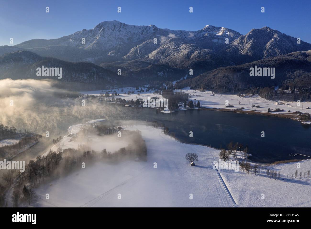 Blick aus der Vogelperspektive auf einen See vor den Bergen im Winter, Schnee, Nebel, Morgenlicht, Blick auf Herzogstand und Heimgarten, Kochelsee, Ausläufer der Alp Stockfoto