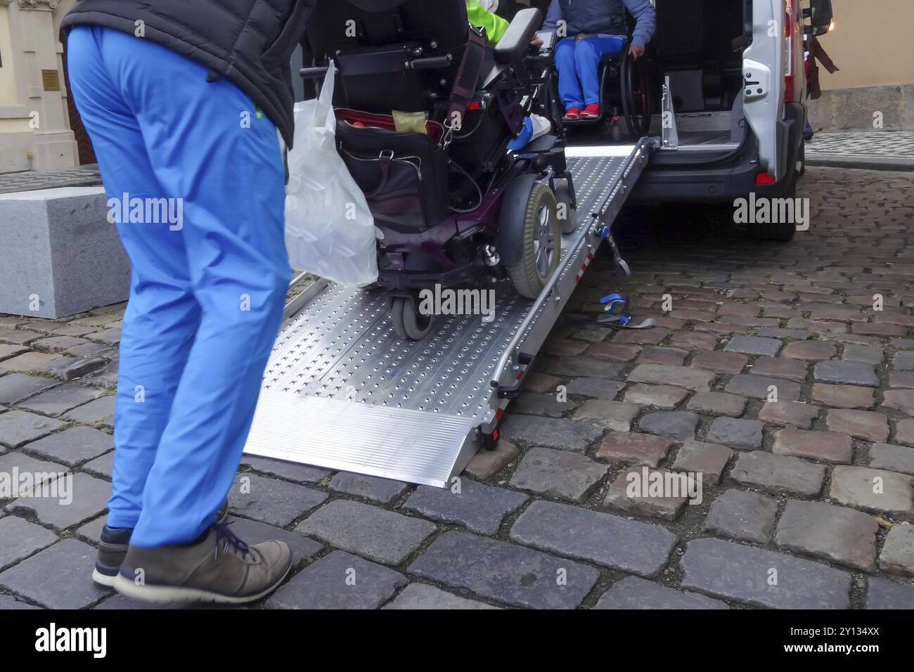 Assistenten helfen behinderten Menschen im Rollstuhl mit Transport über Erreichbare van Rampe Stockfoto