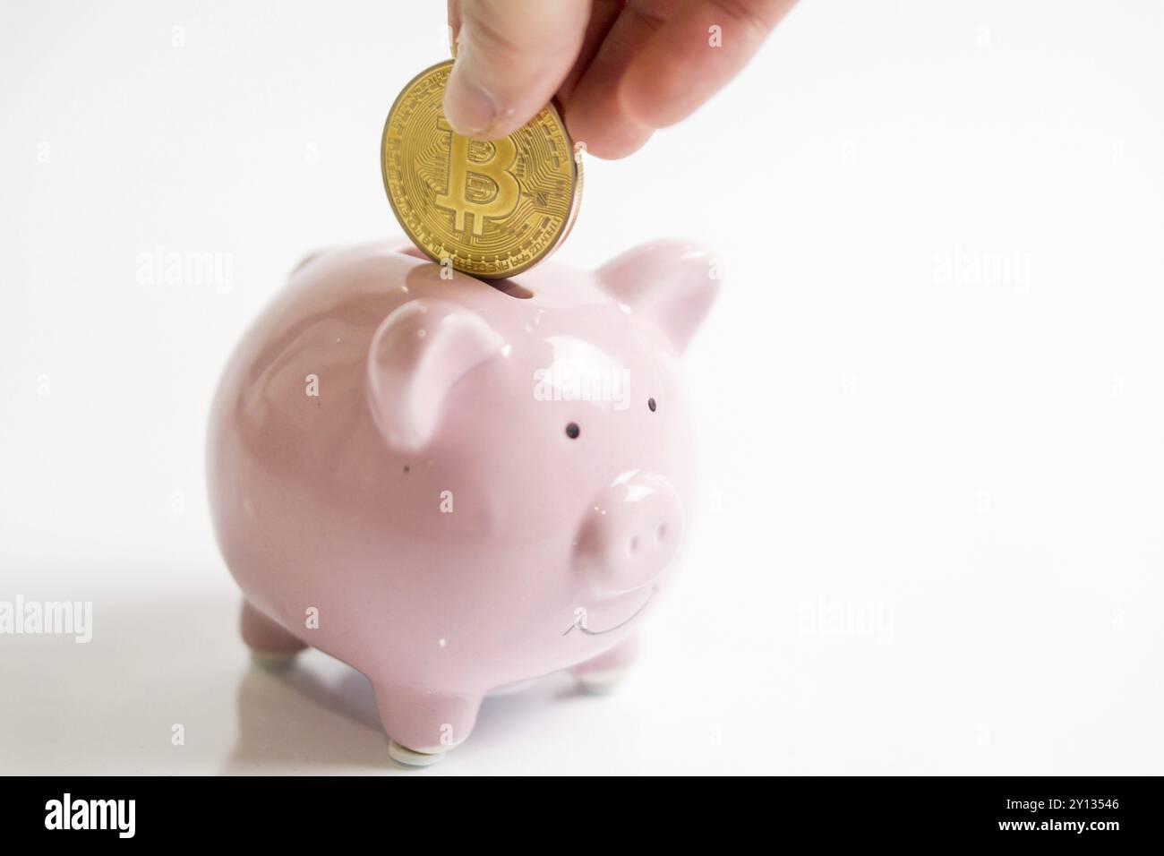 Foto einer Hand, die goldene Bitcoin-Münze in die rosafarbene Geldbox bringt. Schweinebank, Hand hält goldene Bitcoin-Münze virtuelles Geld. Kryptowährung und Speichern c Stockfoto