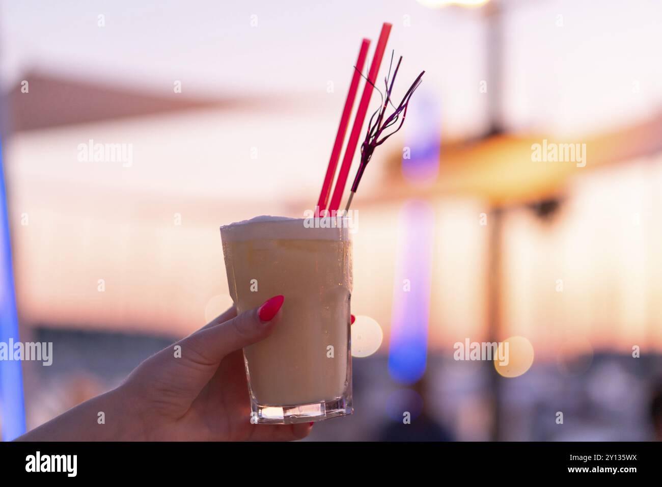 Woman's Hand mit einem Cocktail Glas gegen die untergehende Sonne mit verschwommenen Hintergrund Stockfoto