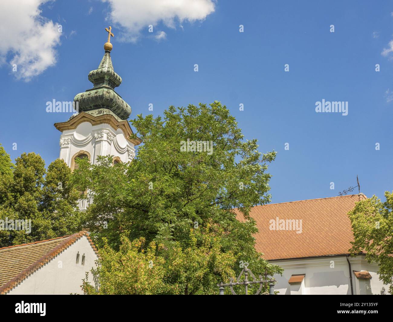 Historisches Gebäude mit markantem Kirchturm und Bäumen unter teilweise bewölktem Himmel, Szentendere, Donau, Ungarn, Europa Stockfoto