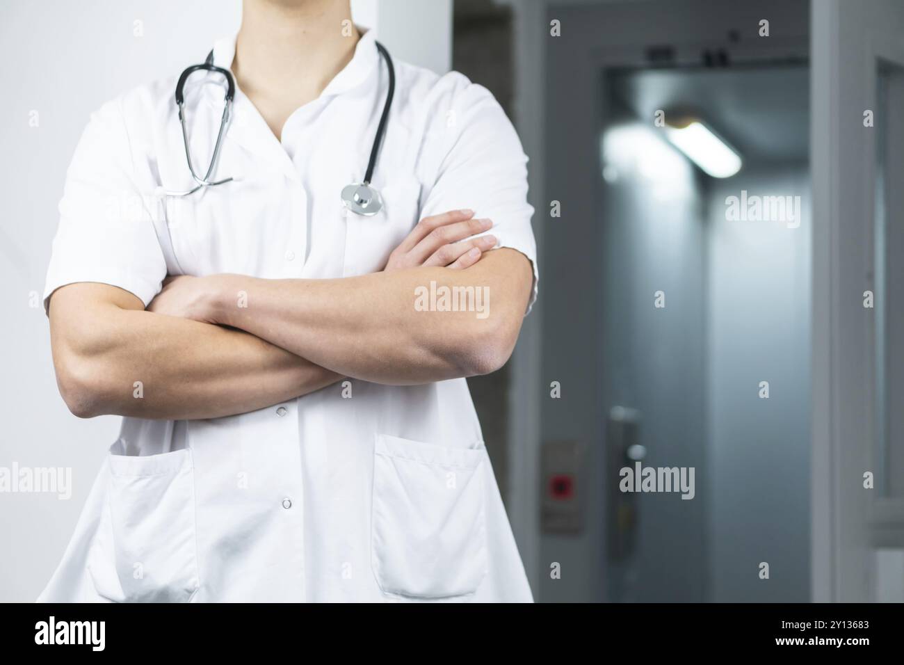 Foto des männlichen Arztes in Uniform mit Stethoskop und überkreuzten Händen, Kopierraum Stockfoto