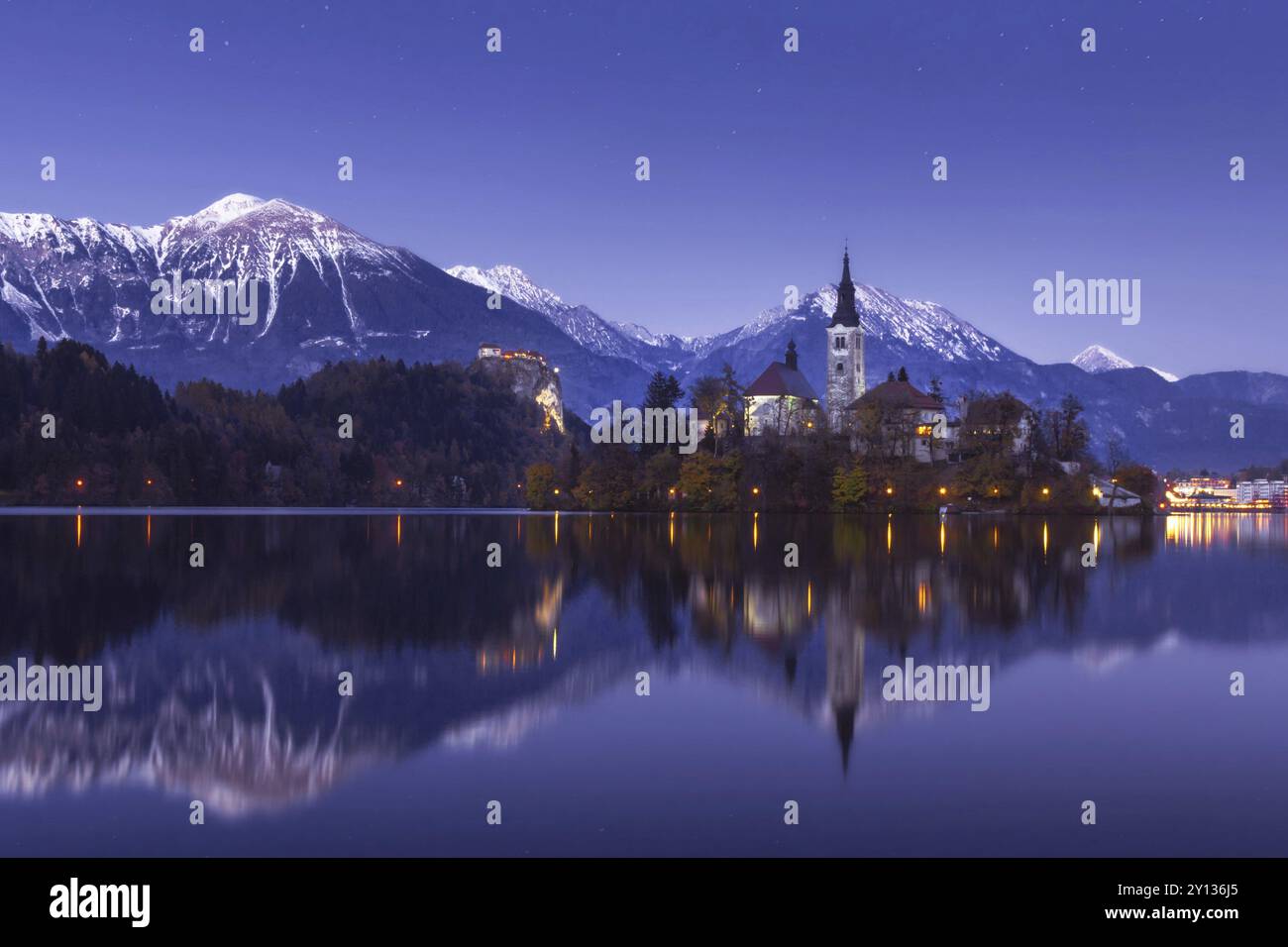 Malerischer Blick auf den See im Winter Nacht mit Castle Rock und St. Martin Kirche unter schöner Sternenhimmel im See Wasser spiegelt Bled Stockfoto