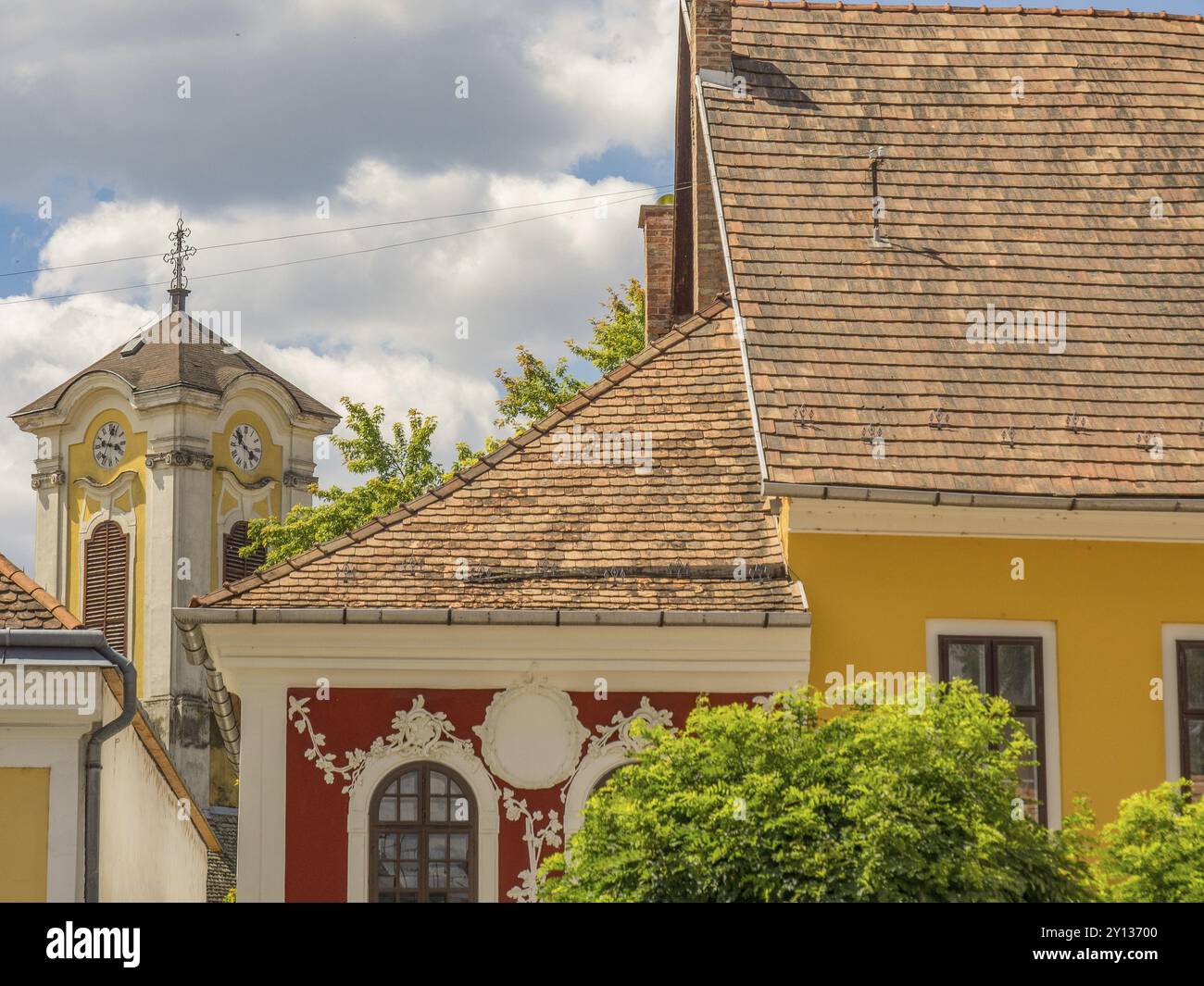 Dorfkirche und farbenfrohe Gebäude mit einem Teil eines Kirchturms unter teilweise bewölktem Himmel, Szentendere, Donau, Ungarn, Europa Stockfoto