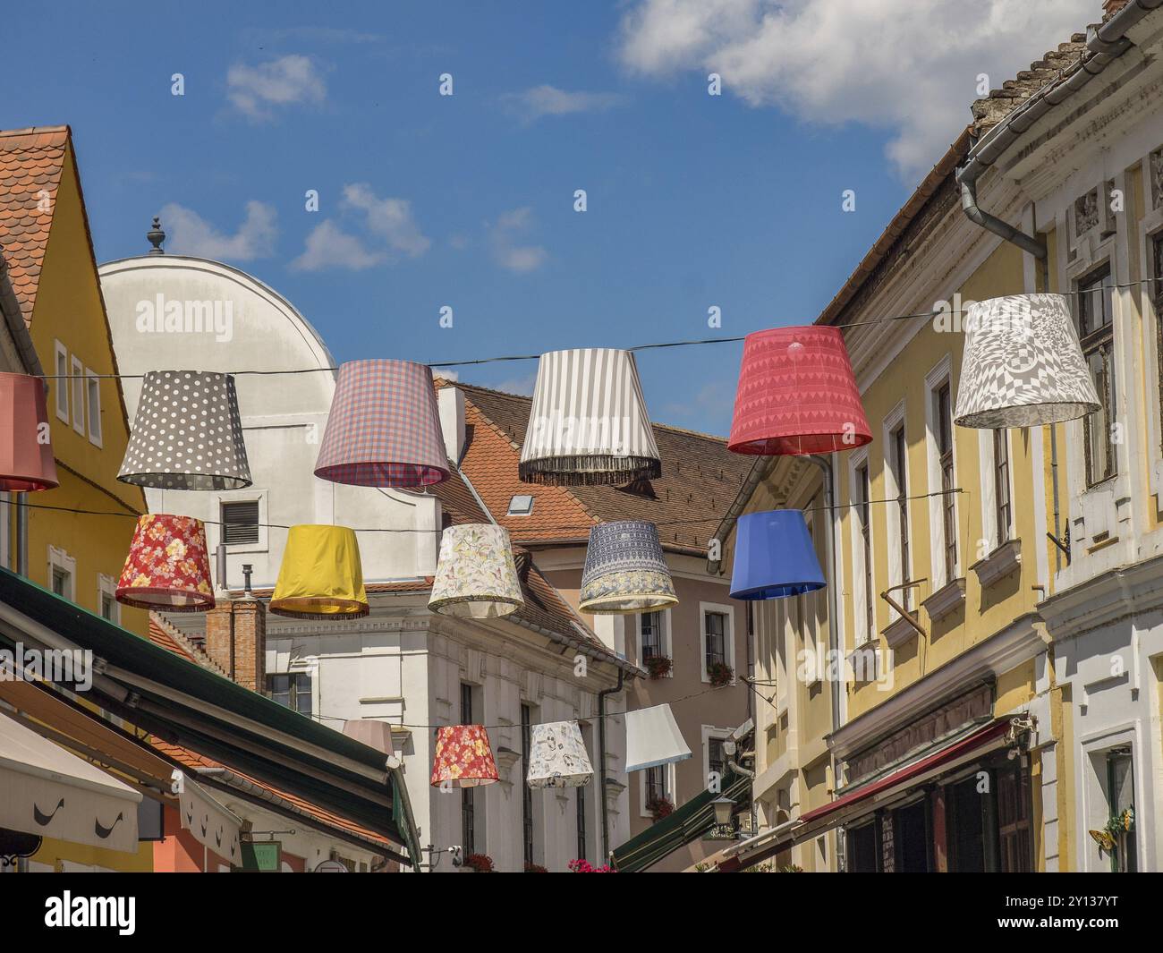 Bunte Lampenschirme zieren eine lebhafte Straße mit historischen Gebäuden unter sonnigem Himmel, esztergom, donau, ungarn Stockfoto
