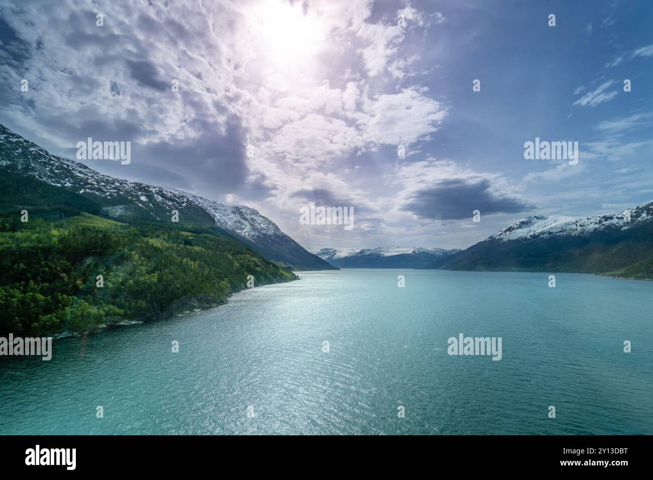 Ein ruhiger Blick auf den Hardangerfjord. Das türkisfarbene Wasser spiegelt die umliegenden schneebedeckten Berge und üppig grünen Wälder wider. Eine friedliche Szene Stockfoto