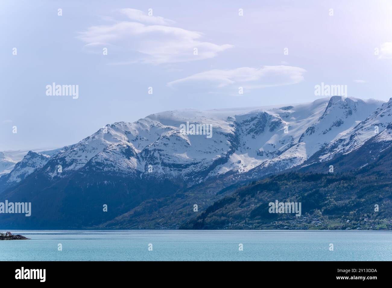 Ein ruhiger Blick auf den Hardangerfjord. Das türkisfarbene Wasser spiegelt die umliegenden schneebedeckten Berge und üppig grünen Wälder wider. Eine friedliche Szene Stockfoto