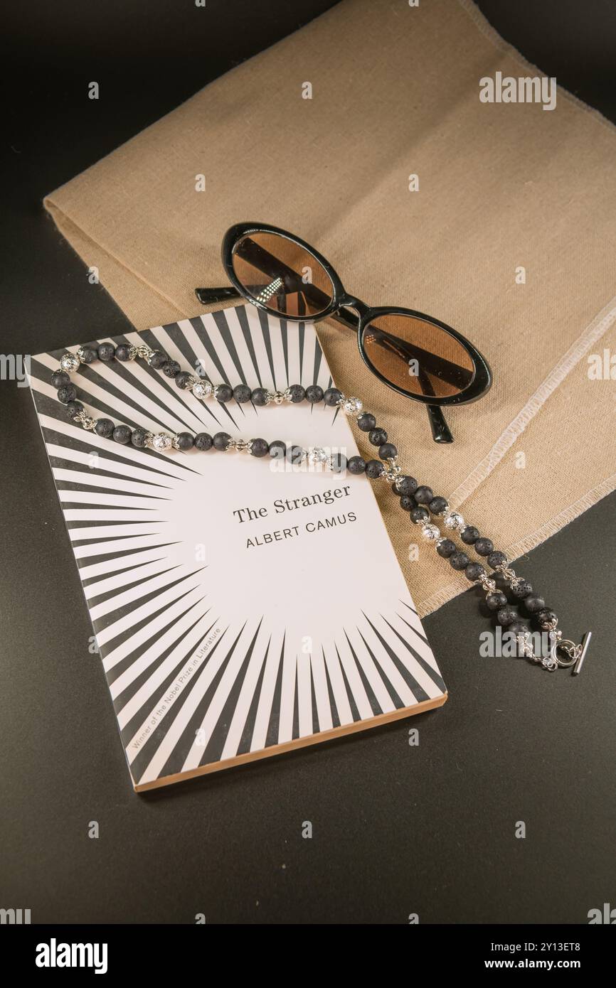 Handgemachte Halskette aus Silber und Vulkanstein auf einem Buch mit Sonnenbrille auf schwarzem Hintergrund Stockfoto