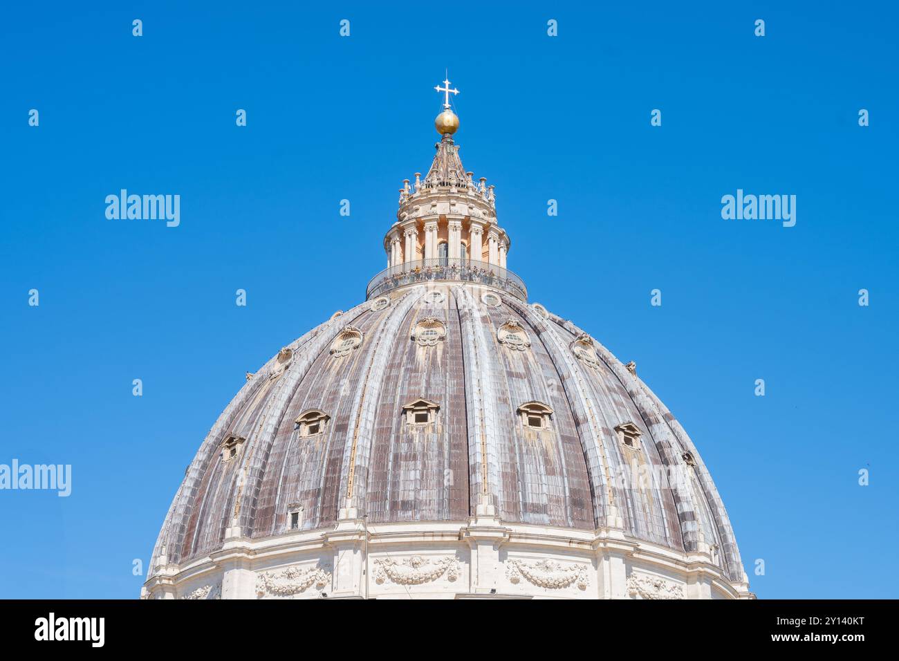 Die majestätische Kuppel des Petersdoms erhebt sich vor einem hellblauen Himmel und zeigt exquisite architektonische Details und das berühmte Kreuz darüber. Es steht als Symbol für Glauben und Größe. Stockfoto