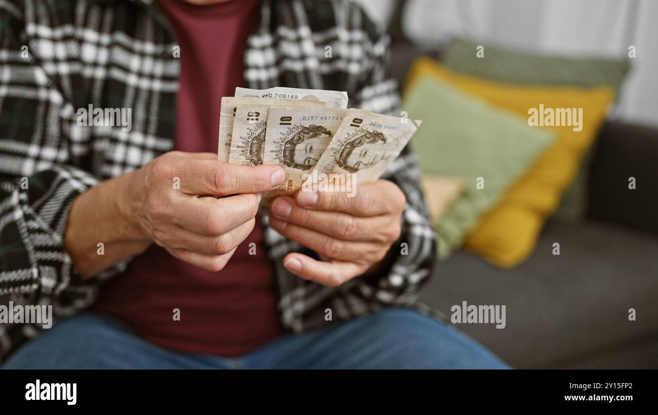 Ein reifer Mann, der britische Pfund in einem gemütlichen Wohnzimmer zählt, bedeutet Finanzplanung. Stockfoto