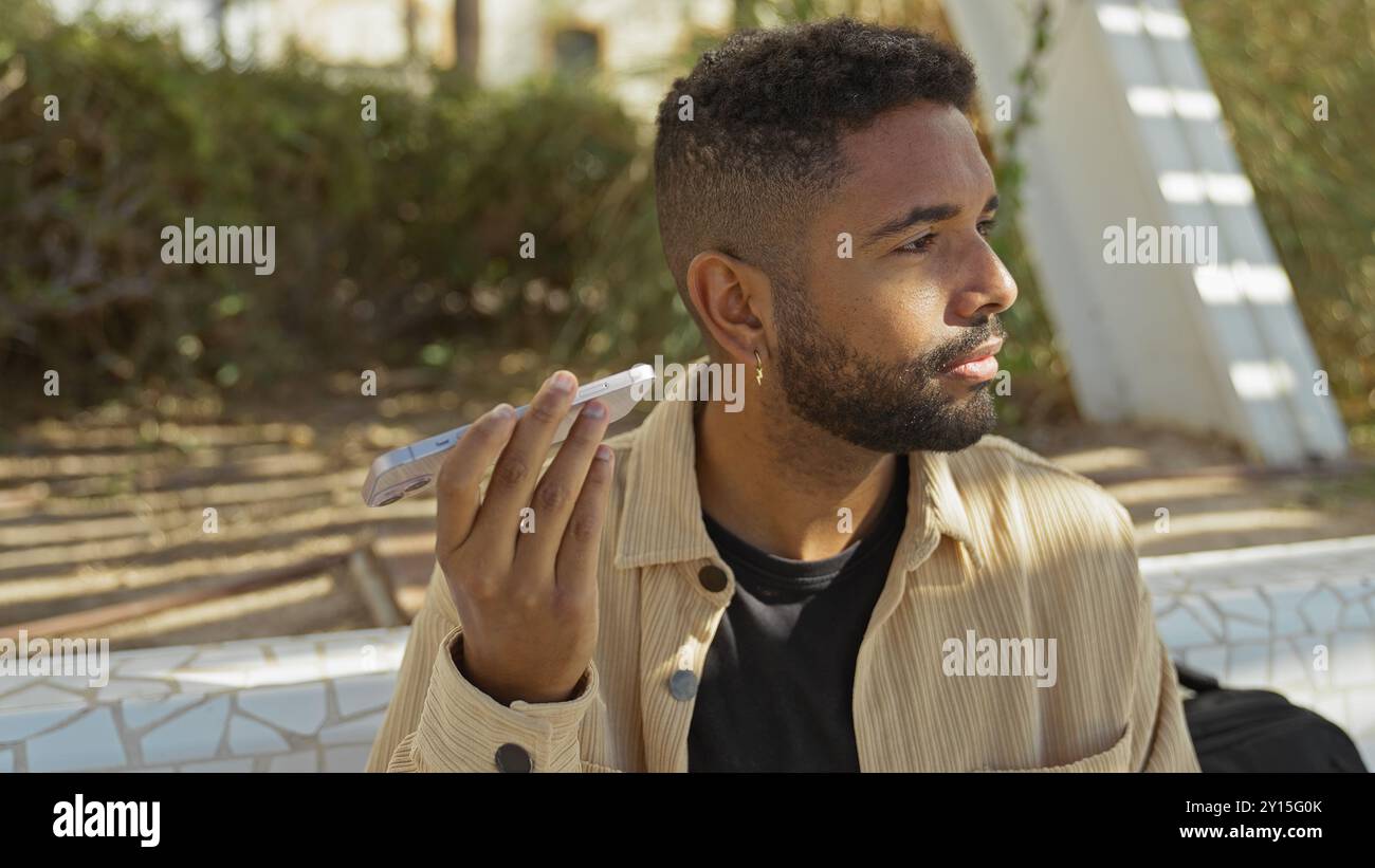 Hübscher junger afroamerikaner mit Bart, der eine Sprachnachricht in einem urbanen Park hört Stockfoto