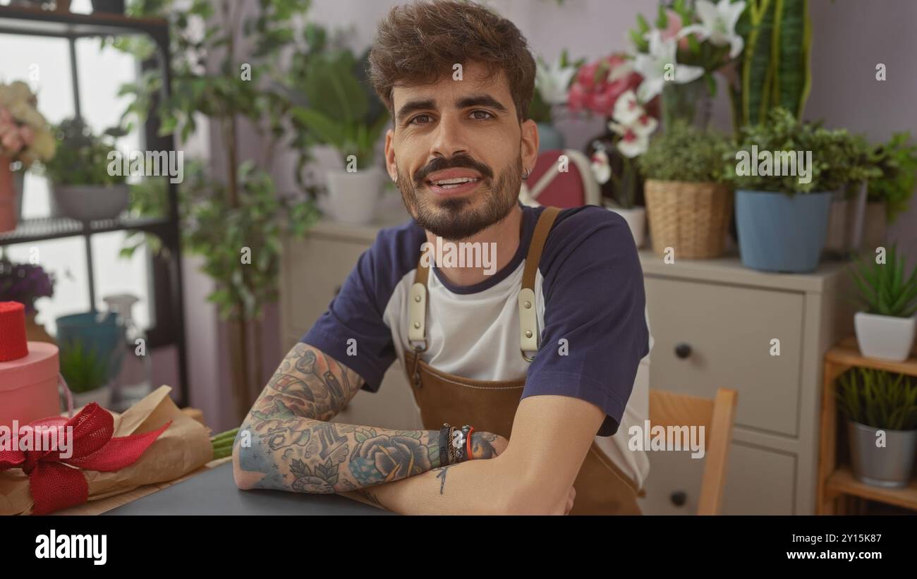 Hübscher hispanischer Mann mit Bart und Tätowierungen, der in einem Blumenladen lächelt. Stockfoto