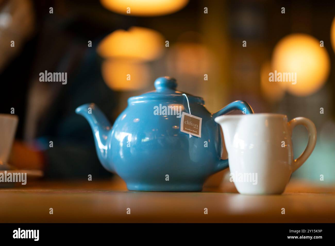 Nahaufnahme einer Teekanne und Milchkanne auf einem Restauranttisch mit dezenter Beleuchtung im Hintergrund. Stockfoto