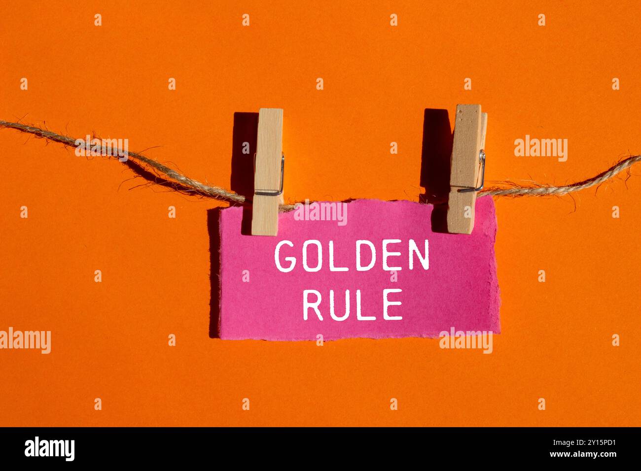 Goldene Regelnachricht auf gerissenem rosafarbenem Papierstück mit orangem Hintergrund. Konzeptionelles goldenes Regelsymbol. Kopierbereich. Stockfoto