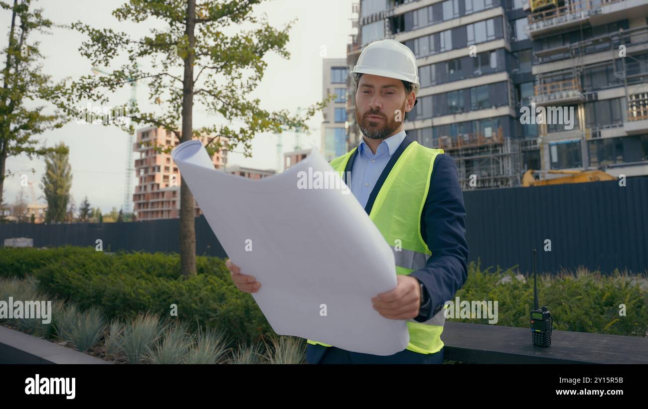 Kaukasischer lächelnder erwachsener Mann in der Stadt mit Blueprint Papier Dokument Plan Arbeit im Freien männlicher Architekt Guy prüft städtische Gebäude Architektur Geschäft Stockfoto