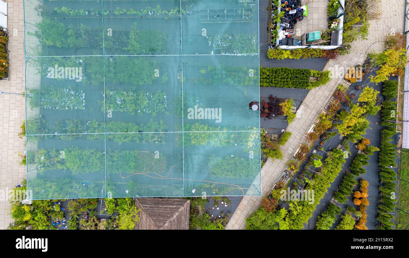 Luftaufnahme einer Gartenanlage mit verschiedenen Pflanzen und Bäumen unter Schutznetz. Wege trennen Abschnitte des Grüns und zeigen eine Vielfalt Stockfoto