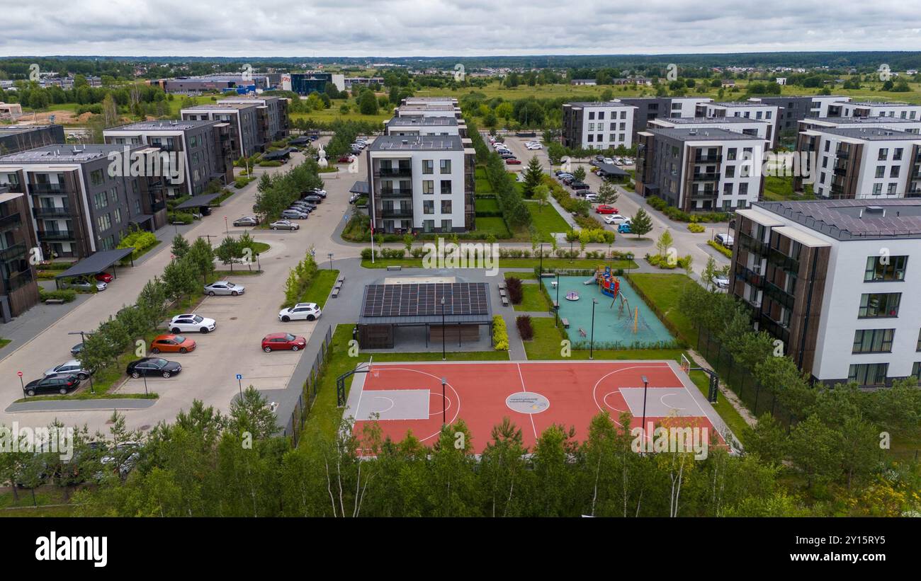 Blick aus der Vogelperspektive auf einen modernen Wohnkomplex mit mehreren Gebäuden, Grünflächen und Parkplätzen. Solarpaneele sind auf den Dächern sichtbar, und ein Bad Stockfoto