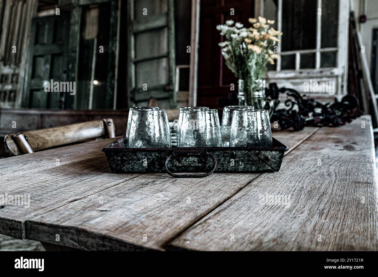 Großaufnahme der Glasbecher in der Blechschale auf dem distanzierten Bauernhof-Tisch mit Holztüren Hintergrund im Farmhouse Style Store Stockfoto