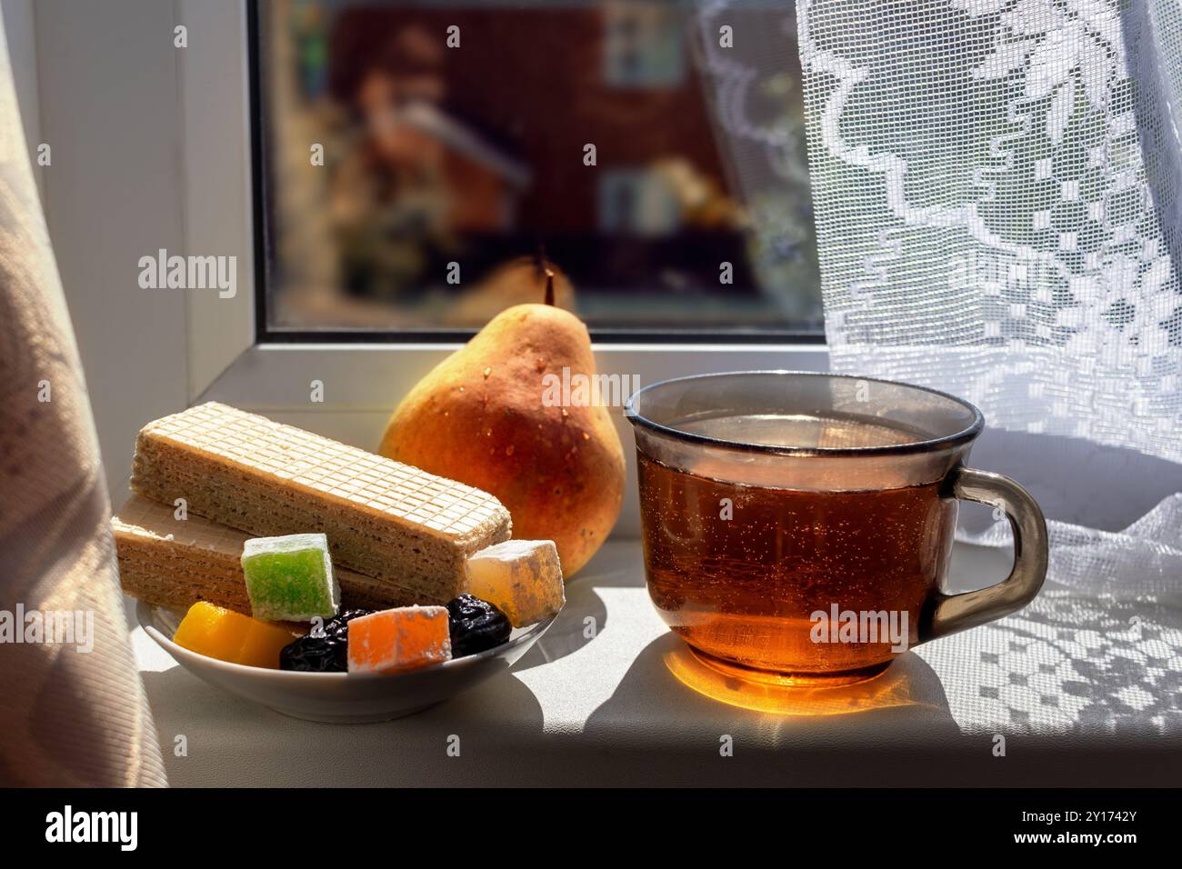 Stillleben auf der Fensterbank des Landhauses am sonnigen Herbsttag. Süßigkeiten, Tee und Birnen am Fenster. Hartes Licht mit gemusterten Schatten aus Tüll. Nahaufnahme. Stockfoto