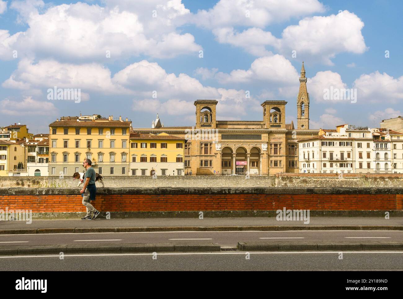 Ein Mann mit seinem Hund spaziert auf dem Lungarno Serristori mit der Nationalen Zentralbibliothek und dem Glockenturm der Basilika Santa Croce, Florenz Stockfoto