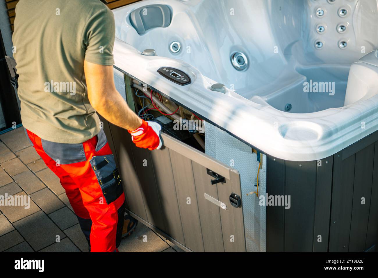 Ein Techniker arbeitet an den Komponenten eines Wannen-Whirlpools, trägt rote Handschuhe und passt die Zugangsklappe in einer häuslichen Umgebung an, um einen sonnigen Tag zu zeigen. Stockfoto