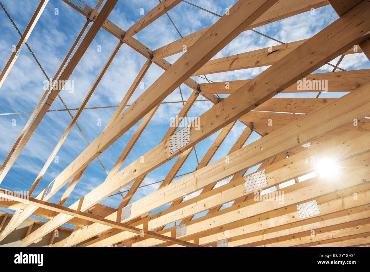 Der Rahmen eines Holzdachs ist vor einem hellblauen Himmel sichtbar und zeigt Balken und Traversen im Bauprozess. Stockfoto