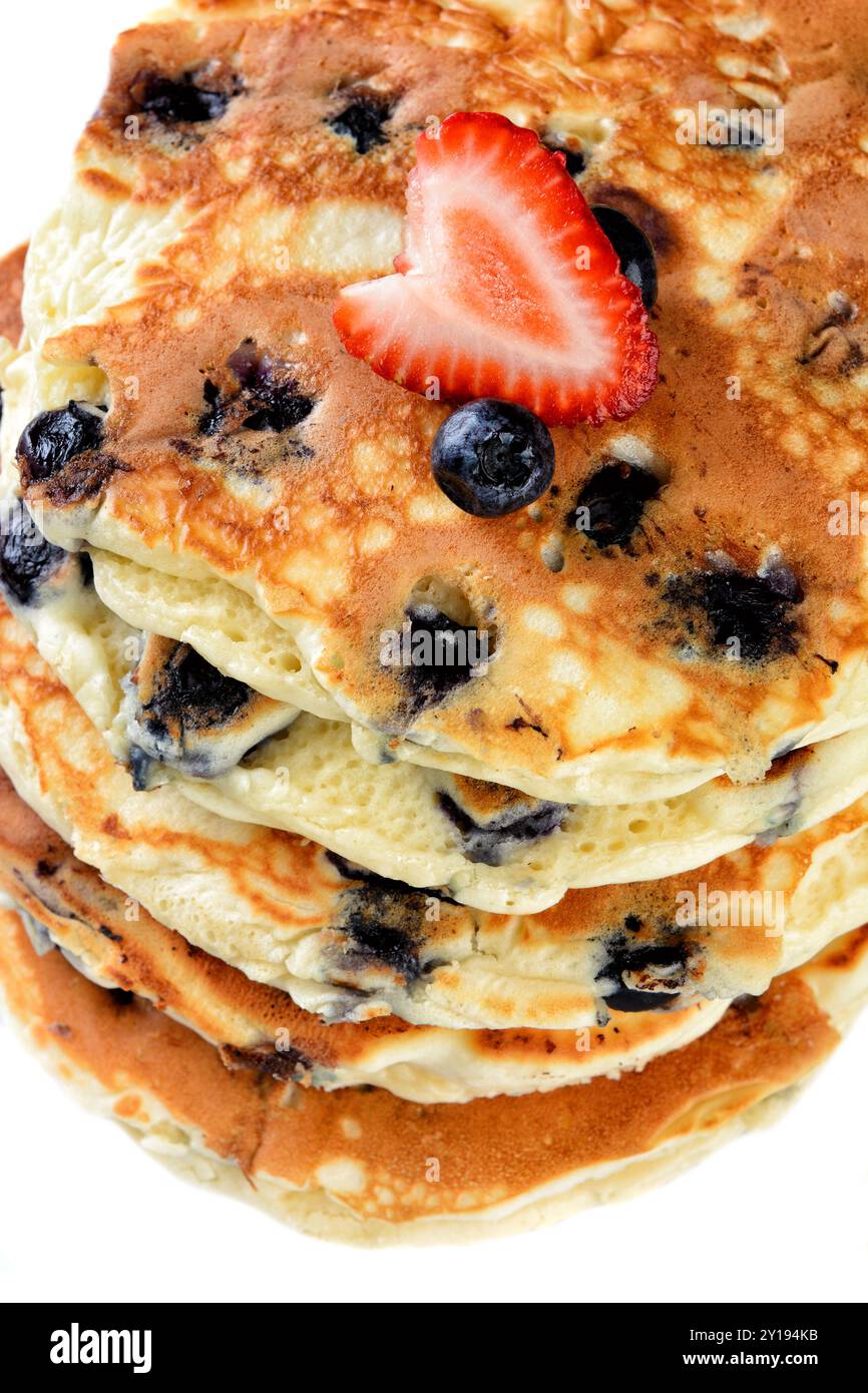 Nahaufnahme eines Stapels frischer hausgemachter Heidelbeerpfannkuchen mit einer Erdbeere auf weißem Teller und rustikalem Holztisch. Stockfoto