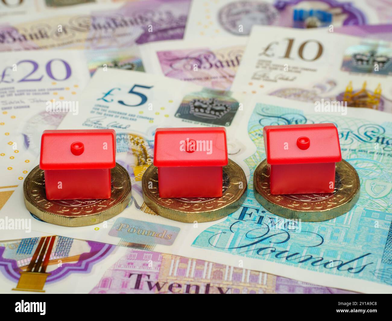 Nahaufnahme von Plastikeigentumshäusern, die auf britischen Pfund-Münzen und Pfund-Banknoten platziert wurden, Bargeld, Großbritannien Stockfoto